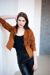 Professional fashion model wearing brown jacket and black outfit posing in studio on clean background, elegant young woman portrait for modeling agency portfolio, modern commercial beauty photography