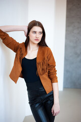 Professional fashion model wearing brown jacket and black outfit posing in studio on clean background, elegant young woman portrait for modeling agency portfolio, modern commercial beauty photography