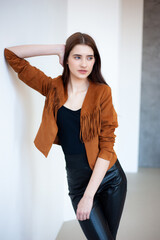 Professional fashion model wearing brown jacket and black outfit posing in studio on clean background, elegant young woman portrait for modeling agency portfolio, modern commercial beauty photography