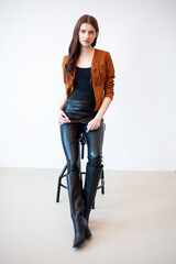 Professional fashion model wearing brown jacket and black outfit posing in studio on clean background, elegant young woman portrait for modeling agency portfolio, modern commercial beauty photography
