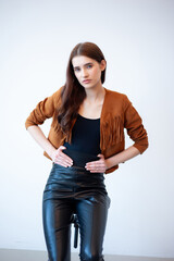 Professional fashion model wearing brown jacket and black outfit posing in studio on clean background, elegant young woman portrait for modeling agency portfolio, modern commercial beauty photography