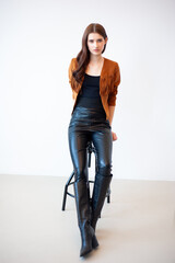 Professional fashion model wearing brown jacket and black outfit posing in studio on clean background, elegant young woman portrait for modeling agency portfolio, modern commercial beauty photography