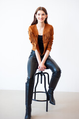 Professional fashion model wearing brown jacket and black outfit posing in studio on clean background, elegant young woman portrait for modeling agency portfolio, modern commercial beauty photography