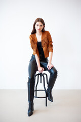Professional fashion model wearing brown jacket and black outfit posing in studio on clean background, elegant young woman portrait for modeling agency portfolio, modern commercial beauty photography