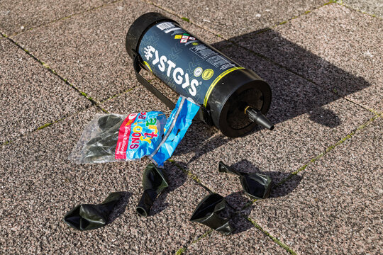 Discarded canister of laughing gas and a package of balloons left on the street, highlighting the issue of nitrous oxide litter.