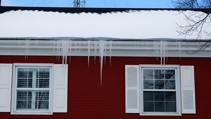 Red house exterior with snow covered roof and icicles hanging over white shutters and windows