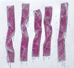 studio photograph of five vertical pink frozen strips encased in clear ice.