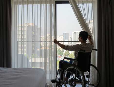 A young asian man in a wheelchair is opening the curtains in a hotel room, looking out at the cityscape through the window, capturing a moment of contemplation and connection with the outside world