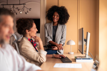 Smiling Black Woman Interacting With Colleagues in Modern Office At Desktop Computer