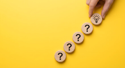 Hand placing idea lightbulb among question marks on wood blocks