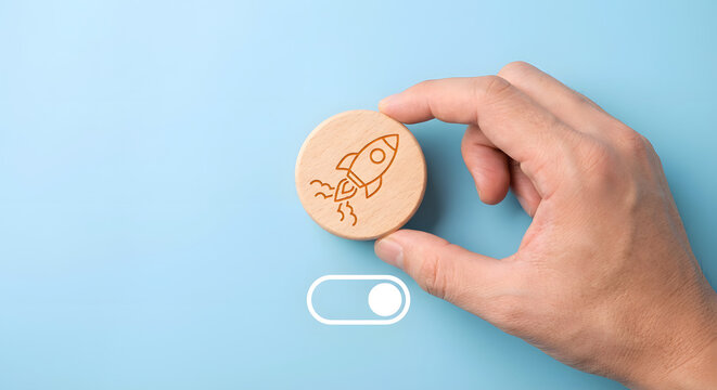 hand holding wooden token with rocket drawing near switch button on blue background