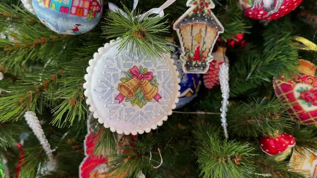 A close-up of handmade cross-stitch Christmas ornament featuring a bells and blue snowflakes hanging on a Christmas tree. All Christmas ornaments embroidered and made by myself.