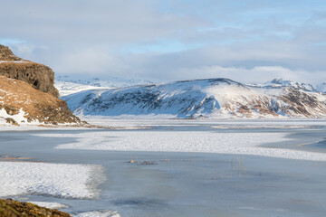 Wonderful Icelandic landscape near Reynisfjara beach. Water surrounded with ice, rocks at the side of the sea. Frozen sea in iceland, rocks and mountains in the distance. Impressive cold winter landsc