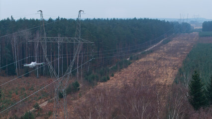 A drone flying past a high-voltage electricity pylon, capturing an aerial view of power transmission infrastructure.