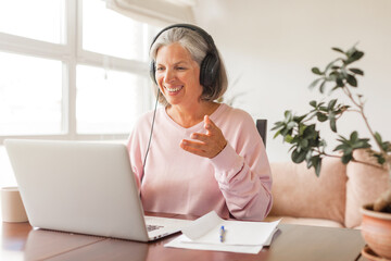 Happy middle aged online course student in headphones learning watching webinar on laptop