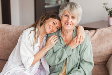 Older mature mother and grown millennial daughter laughing embracing, caring smiling young woman embracing happy senior middle aged mom