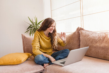 Young smiling woman waving her hand to laptop