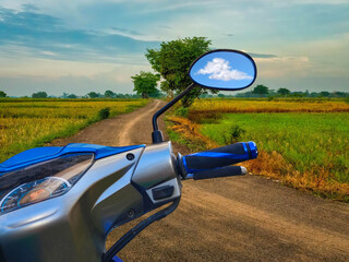 Right rear mirror, handlebars, brake system, and power hand switch motorcycle on a road between the rice fields.