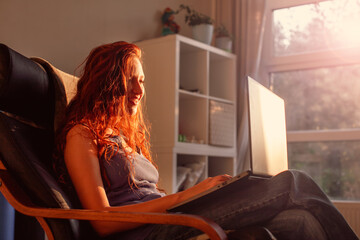 Smiling young woman or teenage girl browsing at his laptop at home