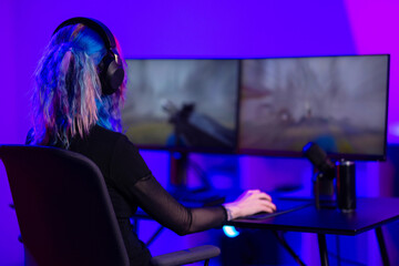 Young female gamer streaming on dual monitors in a colorful gaming setup