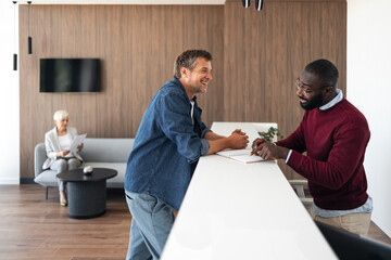 Two Men At A White Counter Discussing Documents In A Modern Office Lobby