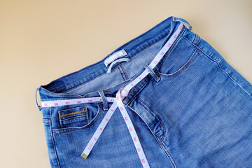 Blue jeans with measuring tape on color background.