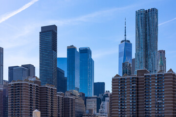 Fototapeta premium The Lower Manhattan skyline features One World Trade Center and glass skyscrapers rising behind brick residential apartment buildings in NYC.