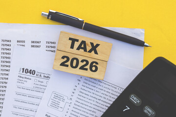 tax preparation setup for 2026 with irs form 1040, calculator, pen, and wooden block on yellow background