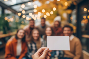 Hand holding a blank card with a group of blurred friends celebrating together