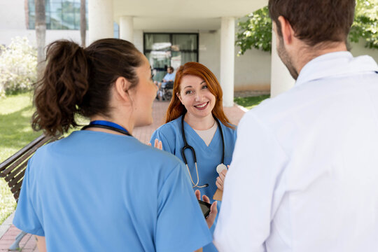 Medical team members with a doctor and two nurses in scrubs having an outdoor discussion at a hospital, demonstrating healthcare teamwork and collaboration in medicine