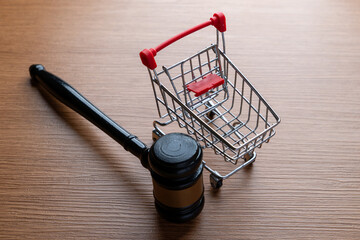 Conceptual image of a shopping cart and judge's gavel on a wooden table. Consumer rights, retail law, e-commerce regulations, consumer protection concept.