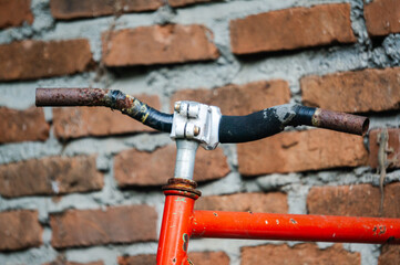 A rusty red bicycle leans against an old brick wall featuring vintage metal plumbing pipes, a blue steel valve, and an industrial water faucet