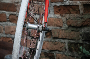 Industrial detail of an old red bicycle wheel leaning against a weathered metal pipe and steel wall in an abandoned factory