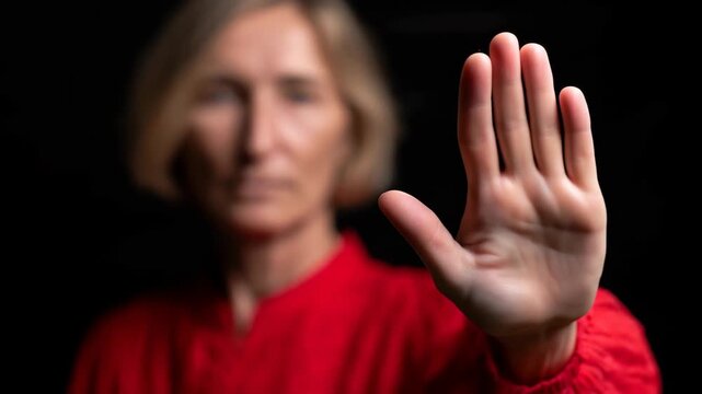 Confident woman in red shirt expressing assertiveness with hand gesture against a dark background