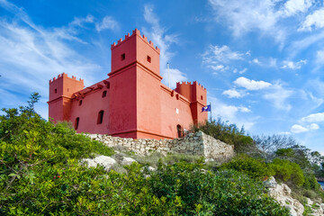 Historic watchtower St Agatha, red painted tower with battlements surrounded by rocks near Mellieha.