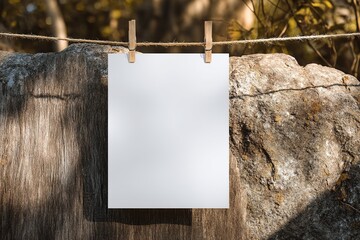 Blank poster hanging on rope above rustic wood and stone surface outdoors
