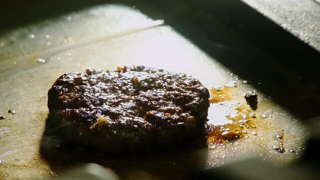 Cook hand covers frying beef cutlet with cheese slice on hot grill closeup. Professional in gloves prepares delicious burger in fast food restaurant
