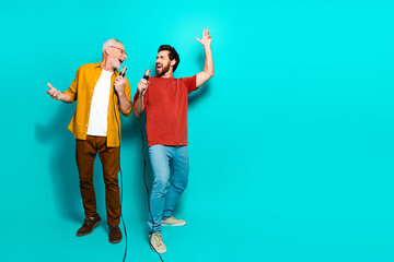 Fototapeta premium Two friends sing together in a bright studio with teal background wearing casual shirts and smiling