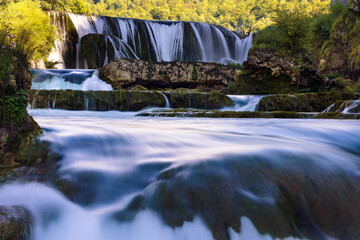 Long exposure river flow below &Scaron;trbački Buk waterfall, silky water over mossy rocks in forest canyon on the Una River, Bosnia and Herzegovina, scenic nature travel background.