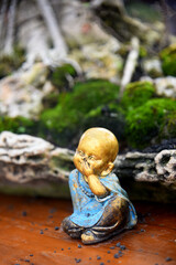 Small and cute Buddha statue, with blurry bonsai tree background