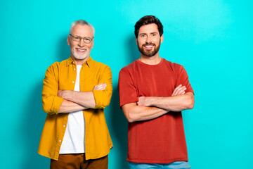 Two men smiling with arms crossed in a bright teal studio setting casual style and family friendly...