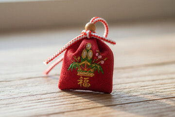 Macro shot of a traditional Japanese New Year charm with hieroglyph "Luck" placed on wood. Soft light creates a calm and symbolic holiday atmosphere.