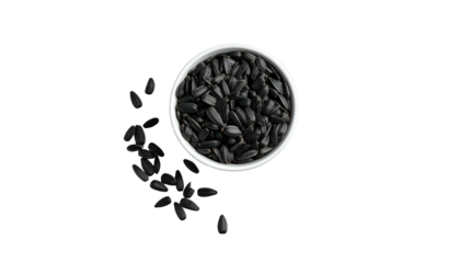 Overhead shot of a white bowl filled with dark, oblong seeds, some scattered around on a stark black background