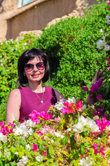 Portrait a woman wearing sunglasses in a bunch of flowers and bright greenery.