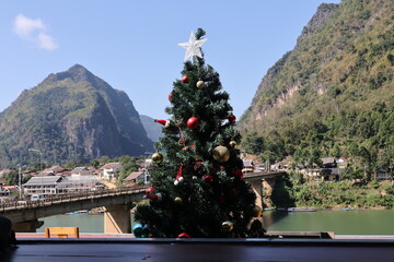 A big blue Christmas tree with a star ornament stands by a Barcelona temple on a bridge, featuring winter holiday lights and festive New Year decorations under a seasonal sky