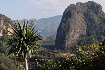 Panoramic autumn mountain landscape featuring a high peak view over a misty forest valley with green trees and a lake under a cloudy sky in Laos
