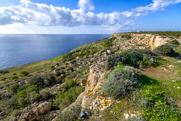Mellieha, Malta &ndash; natural landscape at Ras il-Qammieh with sunlit vegetation, contrasting rock formations, wide sea view and peaceful atmosphere under white clouds