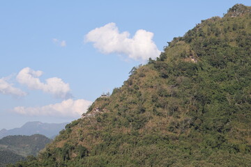 Panoramic autumn mountain landscape featuring a high peak view over a misty forest valley with green trees and a lake under a cloudy sky in Laos