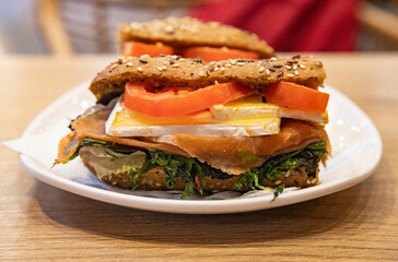fresh sandwich with prosciutto ham, cheese, tomatoes and herbs on a white plate, healthy breakfast