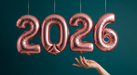 Rose gold balloon numerals spell 2026 against a dark teal background, with a Caucasian hand reaching up, representing upcoming year, celebration